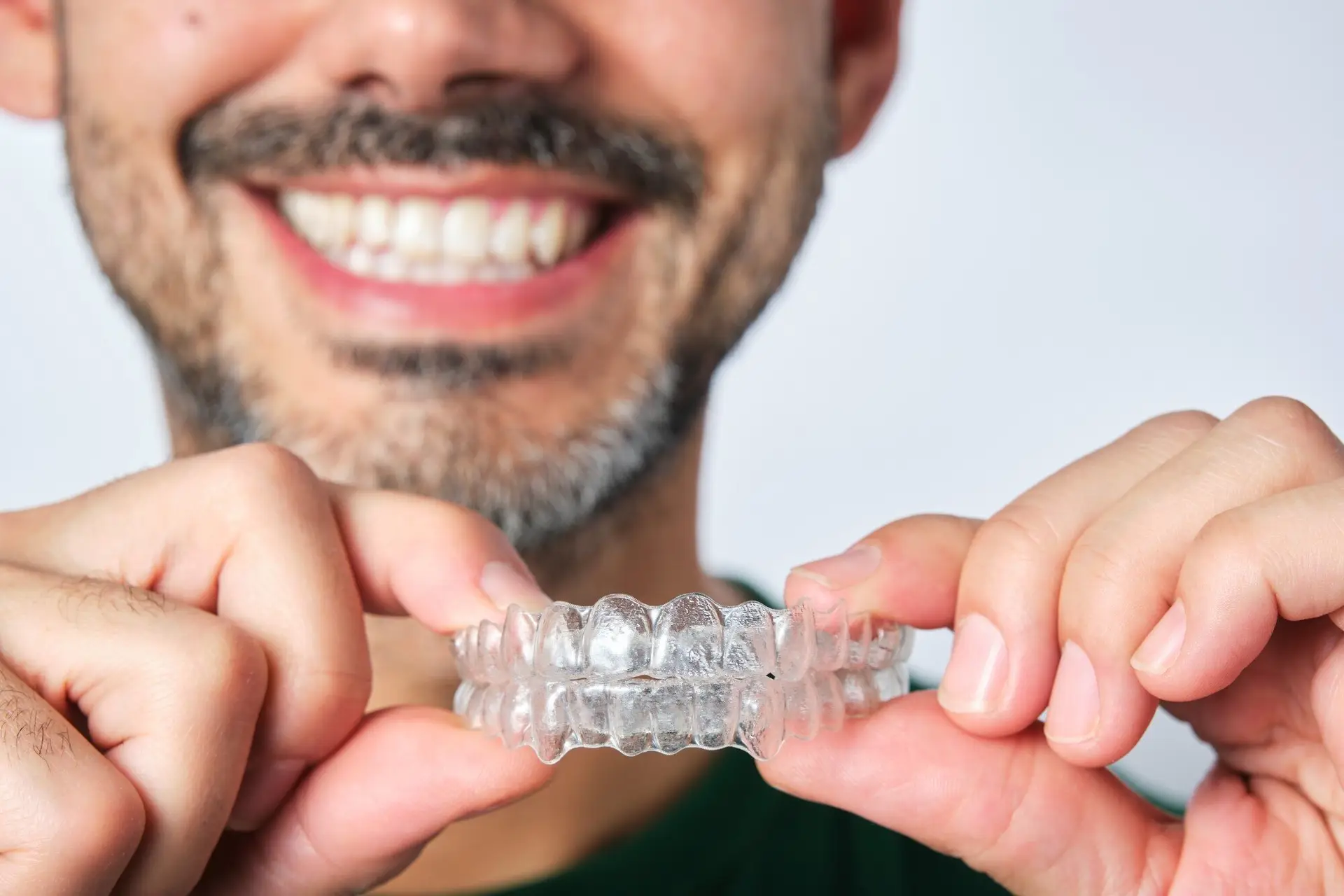 Smiling man holding his upper and lower clear aligners